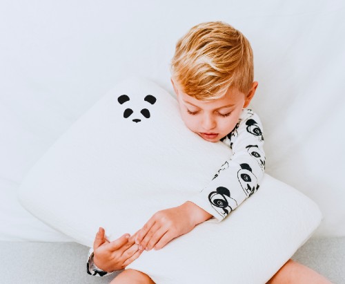Sleepy blonde boy in pyjamas hugging the Panda Bamboo Kids Pillow